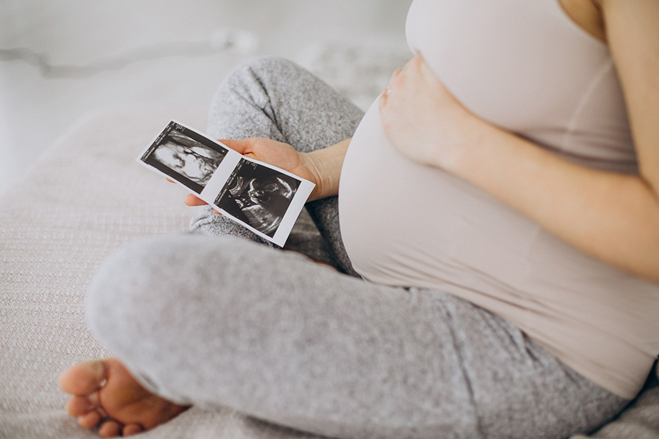 Frau mit Babybauch hält ihren Bauch und ein Ultraschalbild in der Hand
